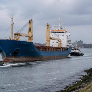 Nave mercantile attraversa il canale di accesso a un porto con mezzi di servizio nelle vicinanze